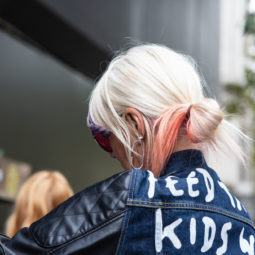 Easy Black Friday hairstyles: Woman with long platinum hair styled into a looped low bun, wearing denim with slogan words on it outside