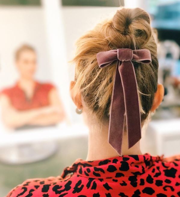 Woman with dark blonde hair styled into a high bun with pink velvet bow under bun
