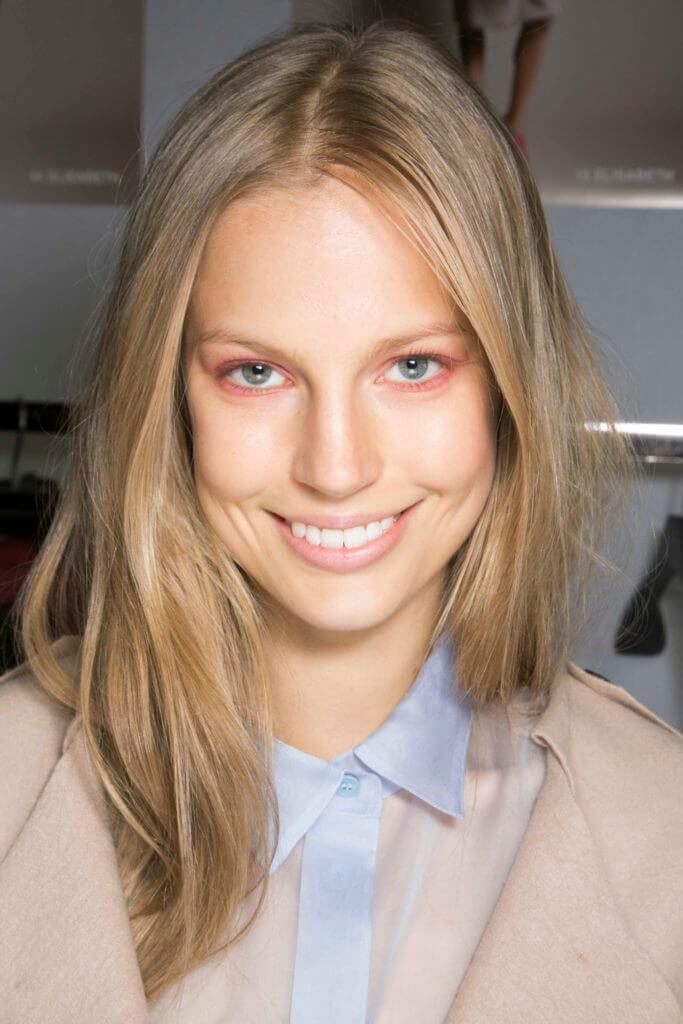 Shades of blonde hair: Woman with straight blonde highlighted hair wearing a light blue shirt with beige jacket.