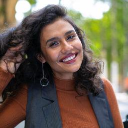 Best brush for curly hair guide: close up shot of woman with natural curly hair, wearing a brown top and grey jacket, wearing drop earrings and posing outside