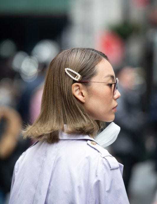 Shades of blonde hair: Woman with dark ash straight bob length hair with flicked out ends wearing a snap clip hair accessory and sunglasses.