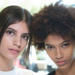 Close up shot of two models one with straight hair and one with afro curls, posing backstage at public school fashion show