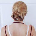 Braided updos for long hair: back shot of woman with long golden blonde fishtail braided bun, wearing red strappy top