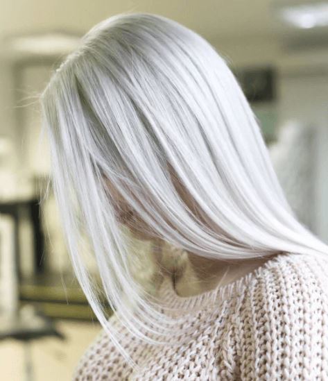 Shades of blonde hair: Woman with long straight ice blonde hair wearing a beige knitted jumper.