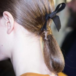 Party hairstyles for medium hair: Brown hair in low ponytail bun with a black bow in backstage image at Rochas FW17 runway show.