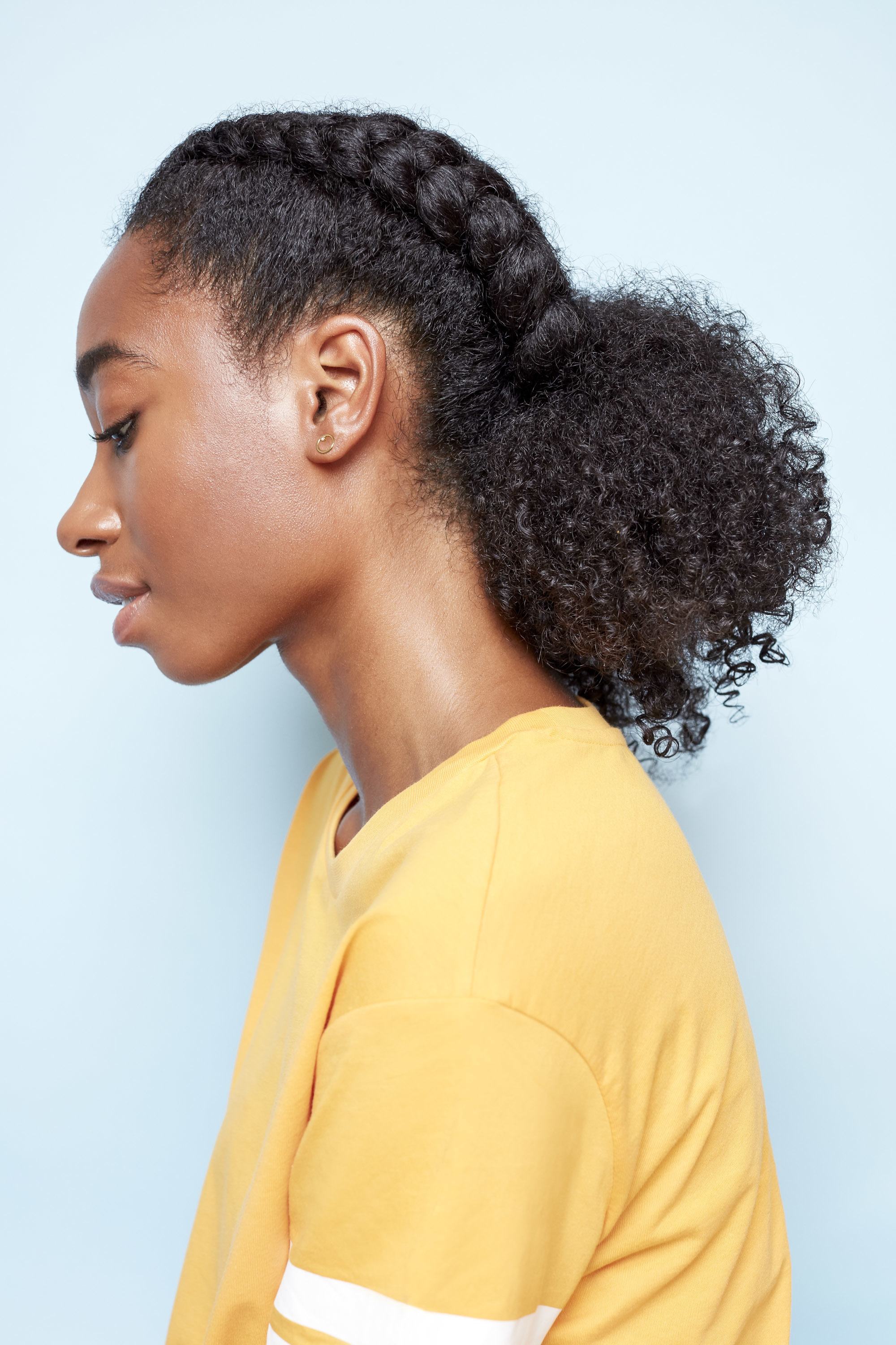 Low manipulation hairstyles: Close up profile shot of a black woman with natural hair styled in two boxer braid ponytails wearing a yellow top