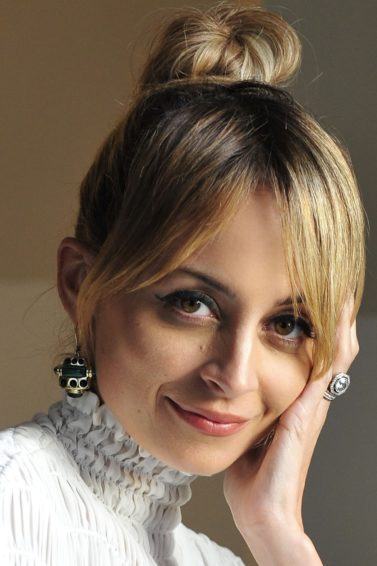close up shot of nicole richie with blonde hair styled into a bun updo, posing and wearing white top