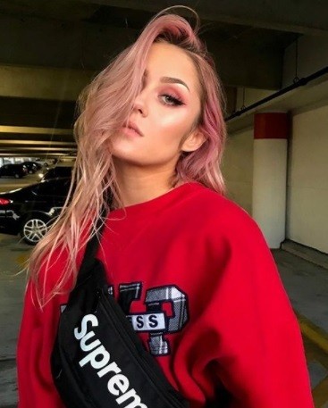 girl with pastel rose gold hair wearing a red sweatshirt with a black supreme bum bag