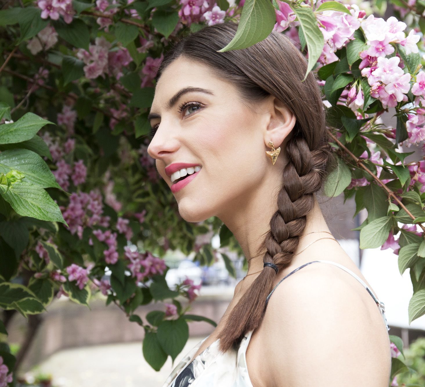 brunette woman with medium length hair styled in a side braid shot outside under trees
