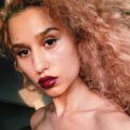 close up shot of raye with blown out natural curls, wearing raspberry lipstick, posing on instagram