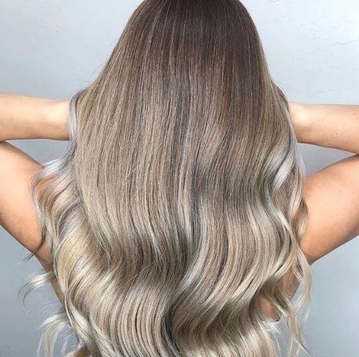 Shades of blonde hair: Woman with long wavy ash blonde balayage hair running her hands through her hair.