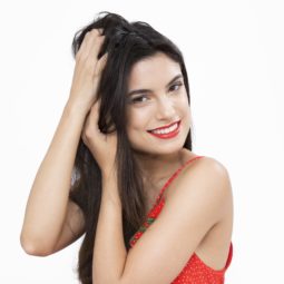 hair tangles guide: shot of model in studio running her fingers through her curly hair, wearing red and posing