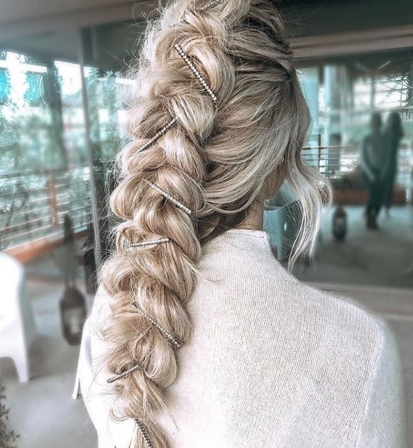 Woman with long bleach blonde hair styled into pull braided ponytail updo with pearl hair slides in it, wearing white jumper and posing in a salon setting
