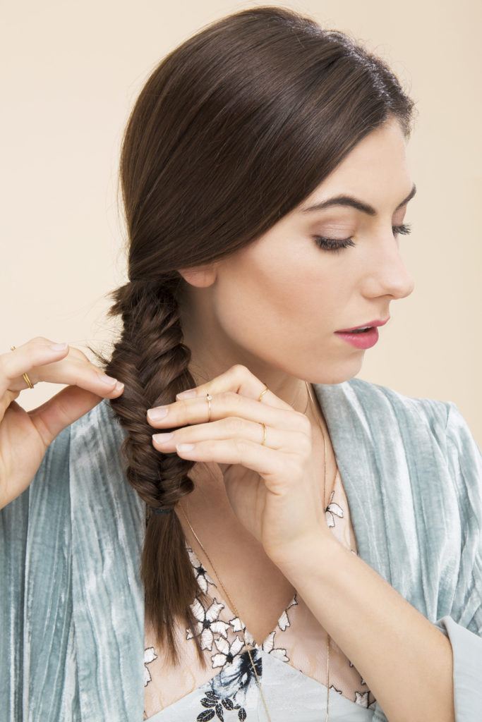 How to do a fishtail plait: Shot of woman pancaking her dark brown fishtail plait in a studio setting