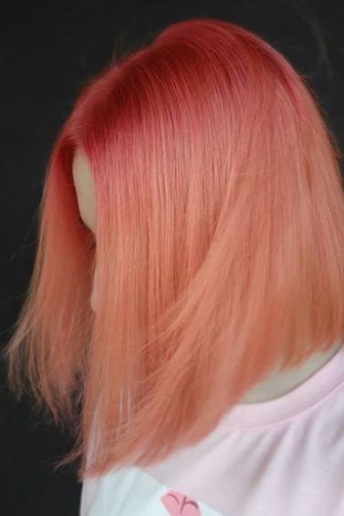 Pantone's Colour of the Year 2019: Close-up of a woman with an angled bob in coral pink ombre, wearing a baby pink t-shirt standing against a black backdrop