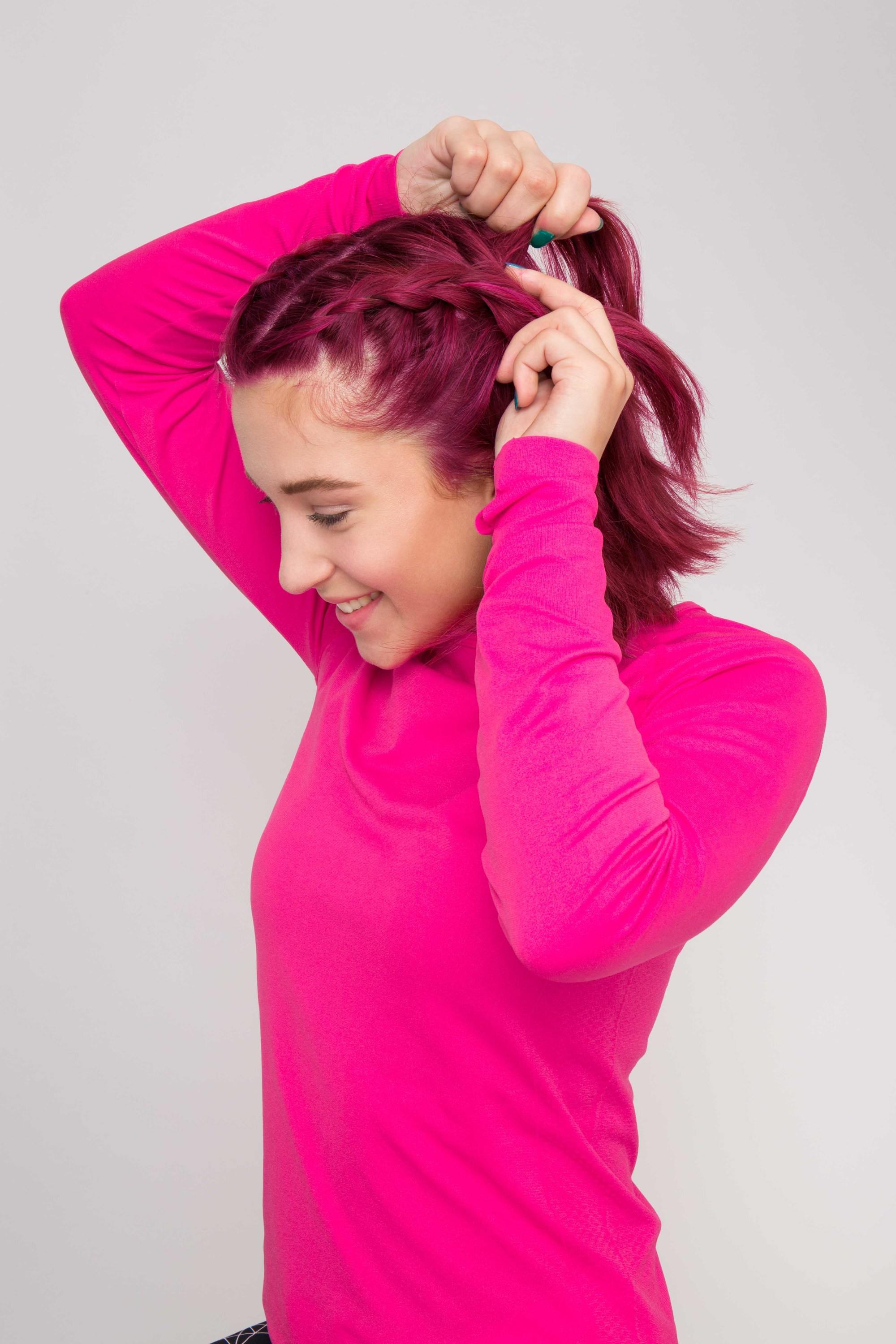How to make your hair wavy without heat: A girl with pink hair wearing a pink top Dutch braiding her hair to make her hair wavy without heat