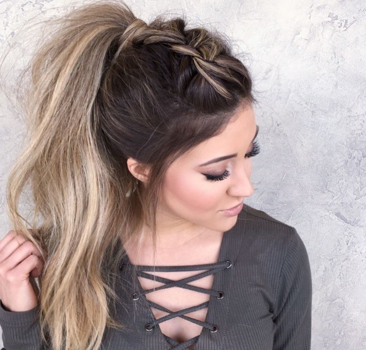 Woman with dirty blonde long hair styled into a messy ponytail updo with a Dutch braid, wearing grey top