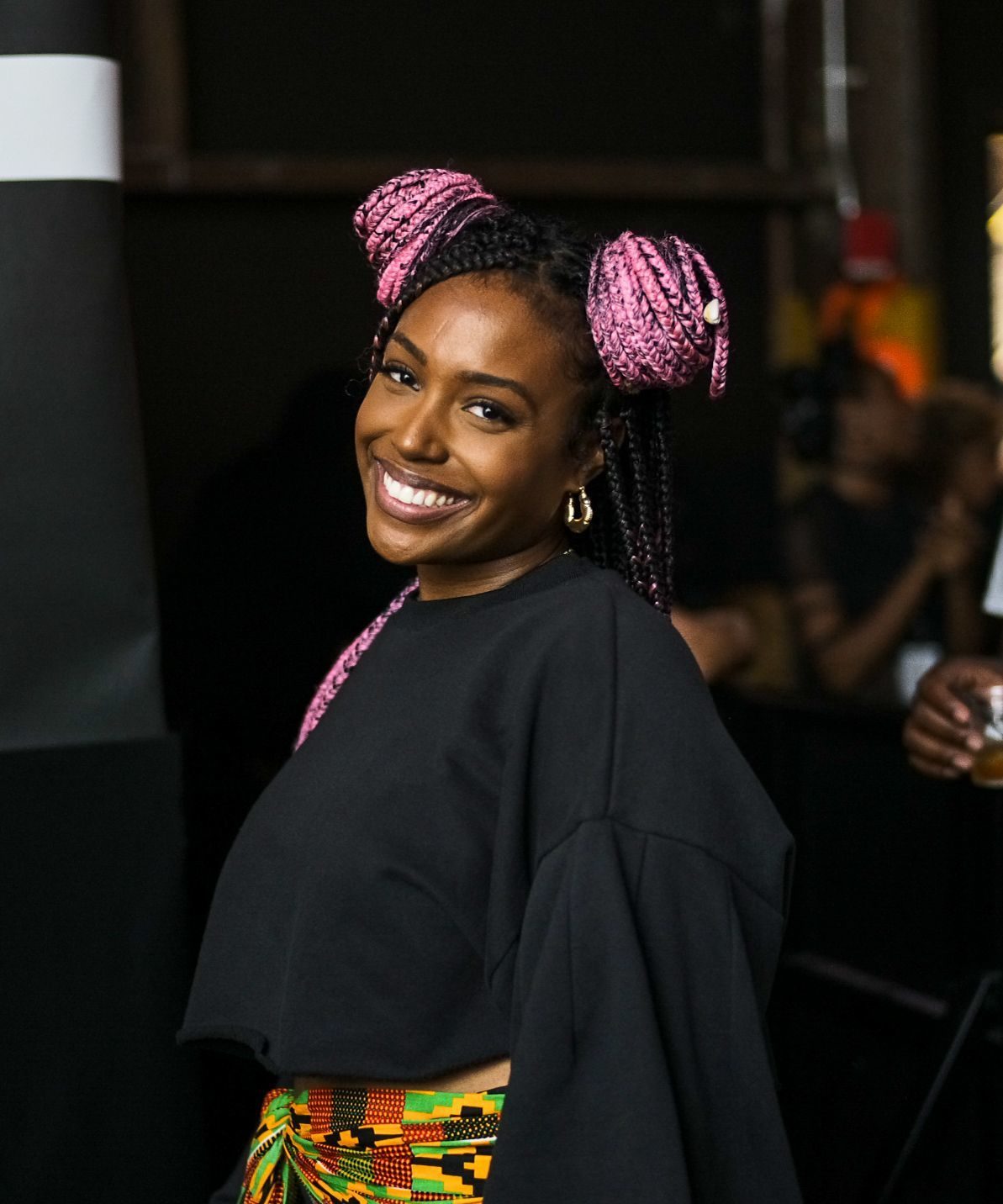 close up shot of scottie beam with block braids styled into a half up half down space bun hairstyle, wearing black and multicoloured skirt