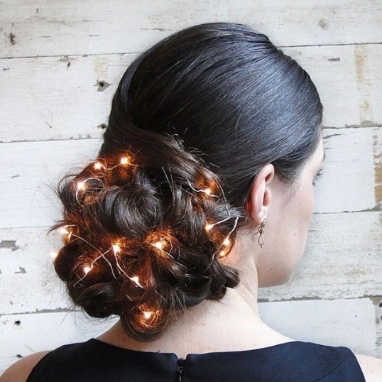 woman with black hair in a big braided updo with fairy lights woven in