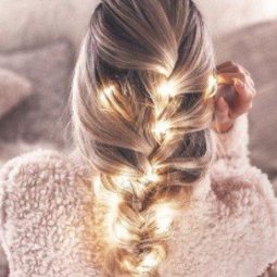 blonde woman in bed with her hair in a thick french braid with fairy lights