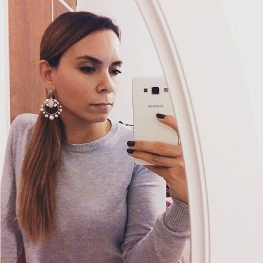 mirror selfie of a brunette woman with long straight hair with her hair in a side low ponytail wearing statement earrings