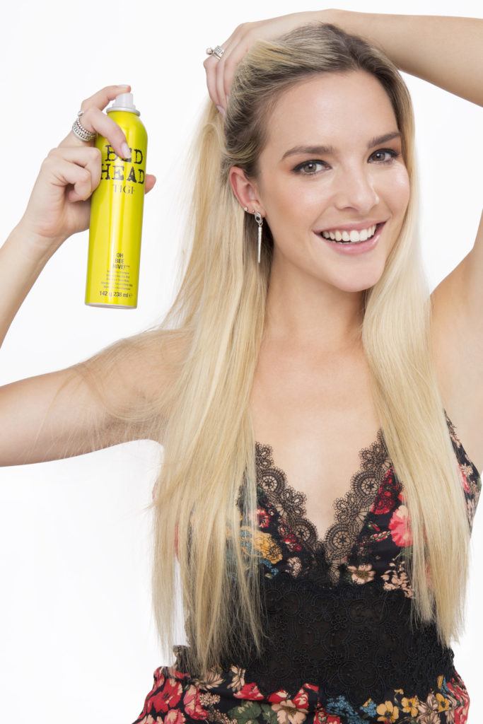 How to do a messy bun with long hair blonde girl spraying dry shampoo smiling