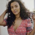 close up shot of maya jama with curly hairstyle. wearing red top and necklace
