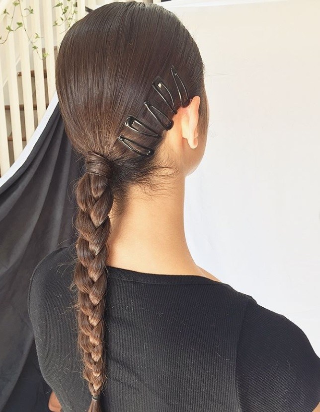 Woman with long dark brown hair styled into braided ponytail updo, with black snap hair clips in it, wearing black and posing in a studio