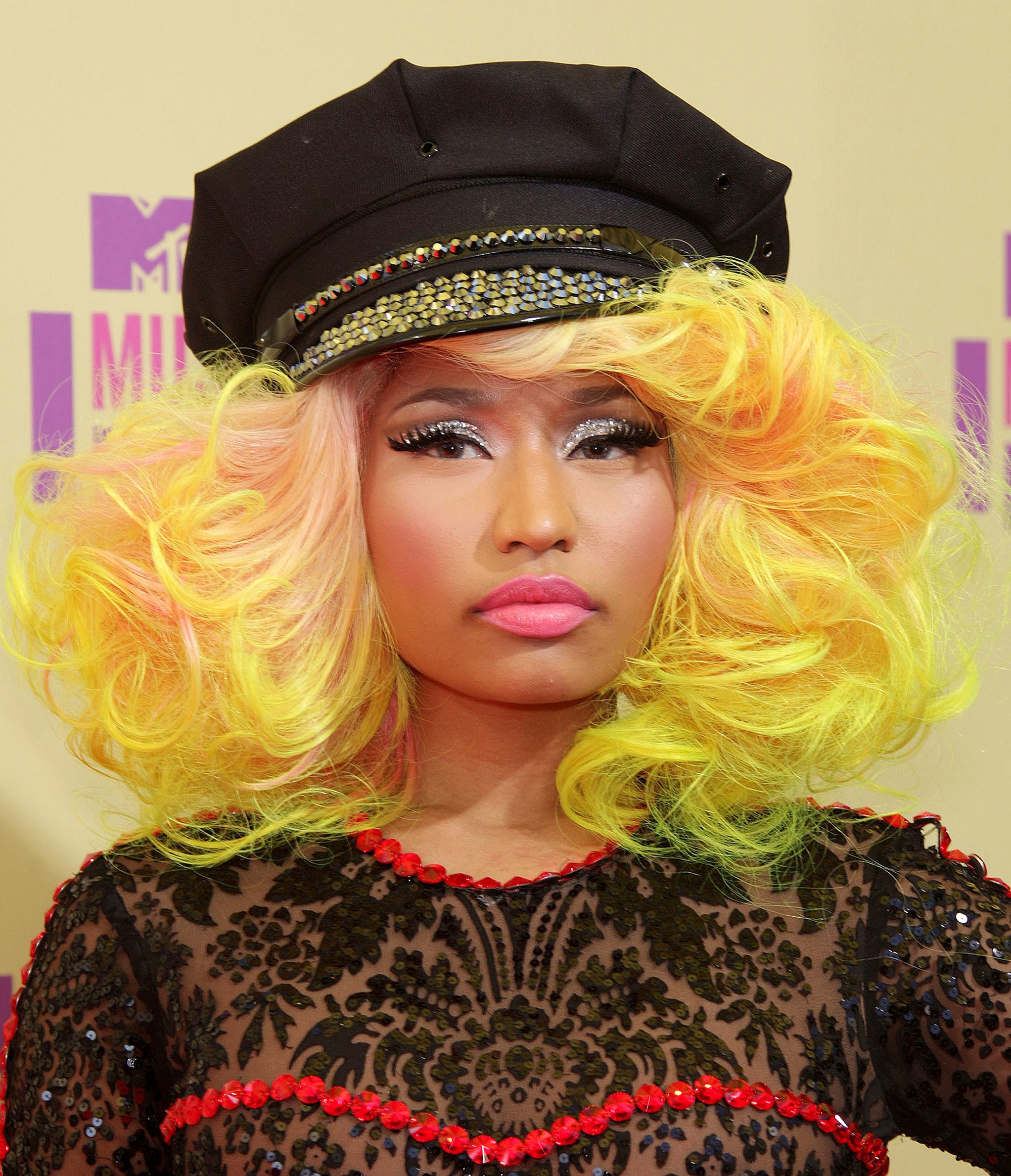 front view of Nicki Minaj with bold yellow and pink curly shoulder length hair with baker boy cap