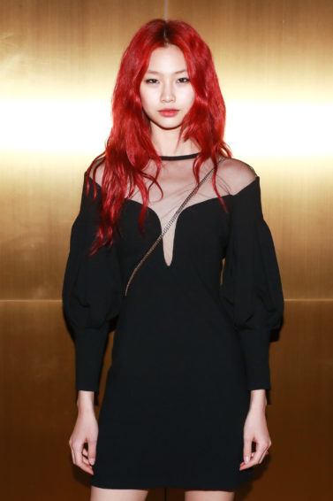 Close up shot of model with red hair, wearing black dress and posing against golden wall