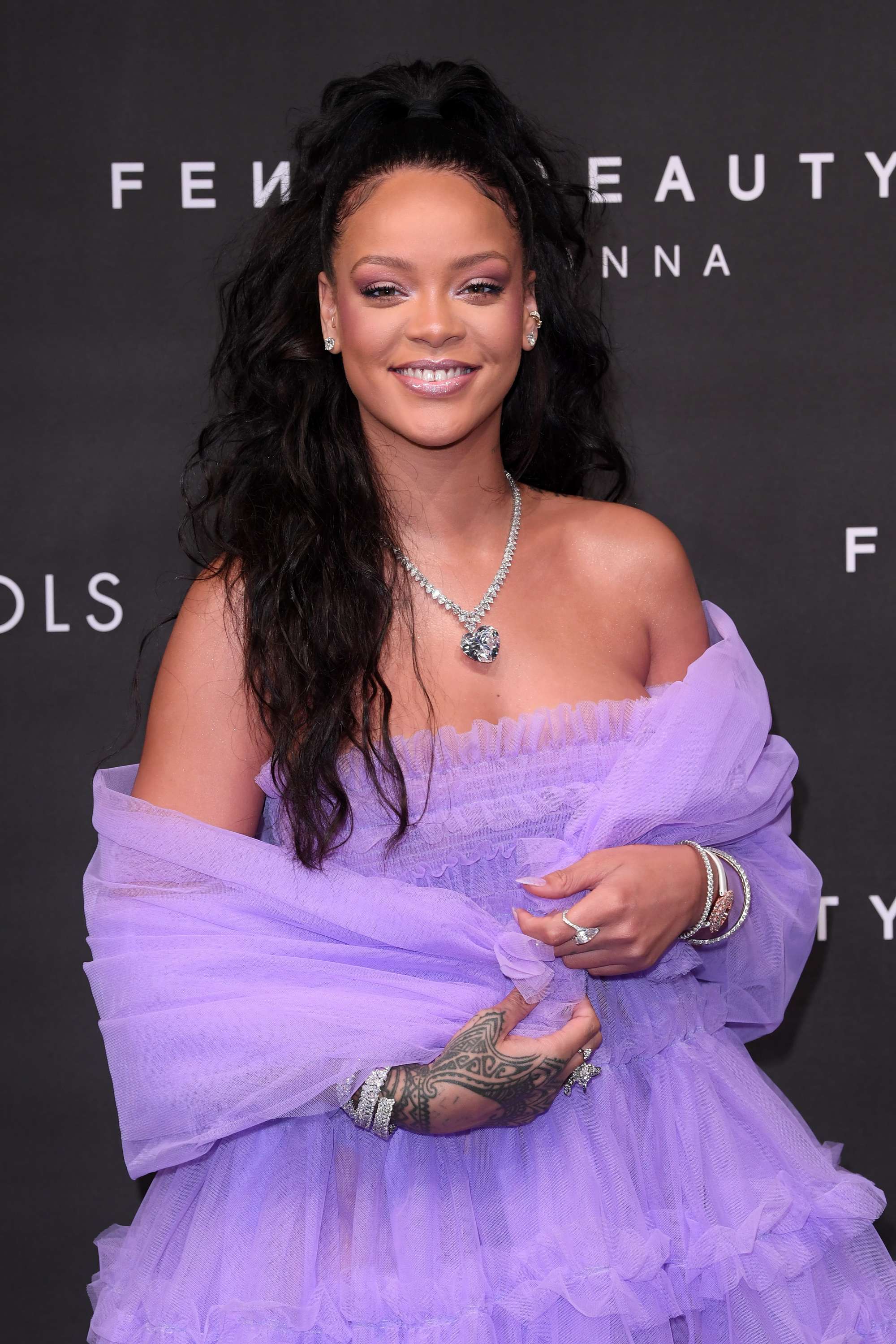 close up shot of rihanna with half up ponytail and curly hair, wearing purple dress and necklace at the fenty beauty launch