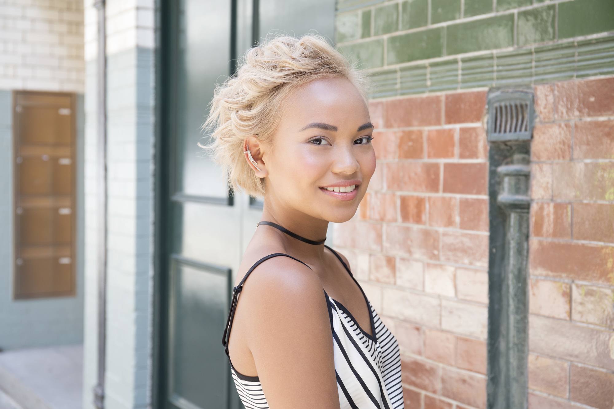 How to curl short hair girl standing near brick wall with curly blonde hair