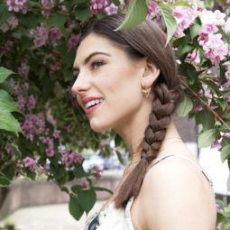 Side braid tutorial girl with brown hair outside smiling near purple flowers