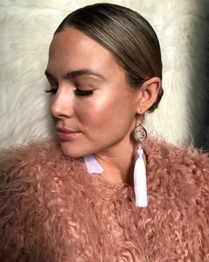 woman wearing a fluffy pink jacket with her brunette hair in a low sleek bun with white tassel earrings