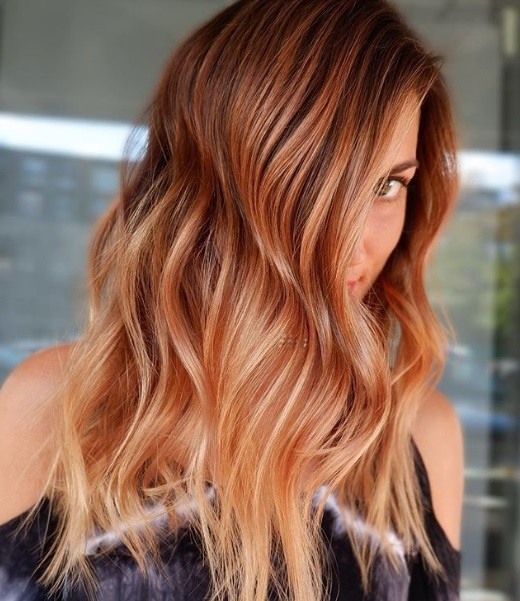 Spiced cider hair: Woman with long, wavy spiced cider pumpkin hair, wearing black and posing in a salon