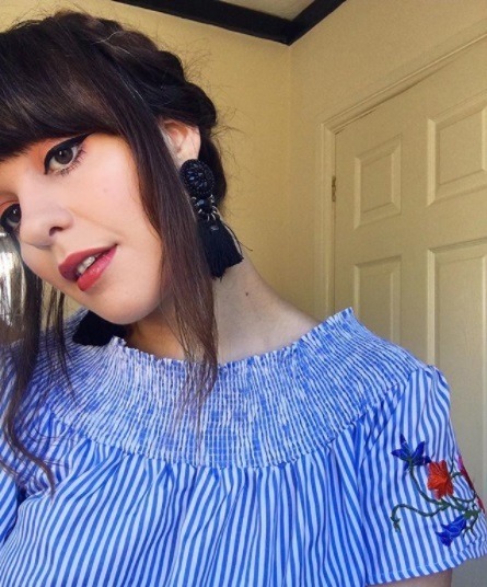 brunette woman in a striped blue top with her hair in milkmaid braids with black earrings