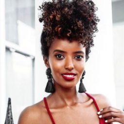 woman wearing a red top with her natural hair in a pineapple updo style with statement tassel earrings