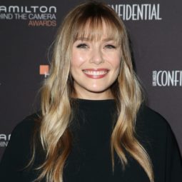 Elizabeth Olsen with long, wavy dirty blonde hair with long and straight feathery bangs, wearing all black on the red carpet