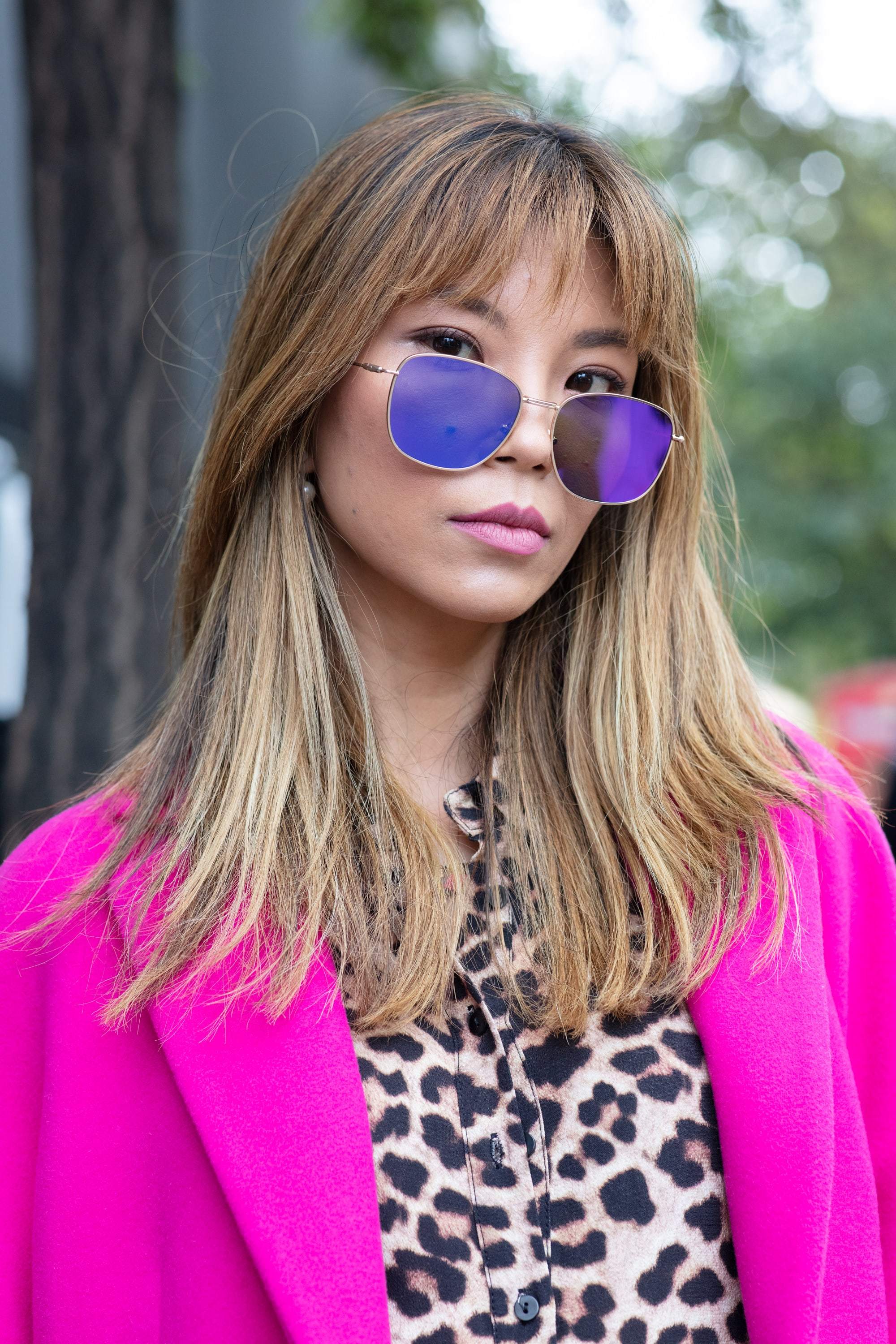 Shot of woman with dark blonde medium hair with sleek, feathery layers in it, wearing sunglasses with hot pink jacket