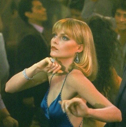 michelle pheiffer in the film scarface wearing a blue silk dress with shoulder length blonde hair and bangs