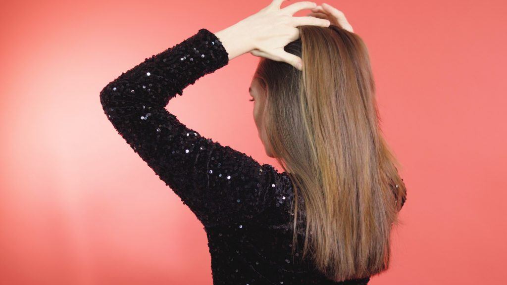 Woman with mid-length brunette hair tying hair into a half-up ponytail