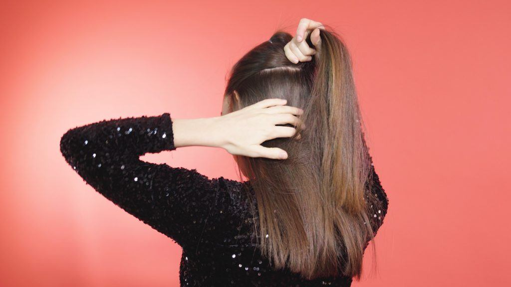 Brunette woman tying a second half-up ponytail