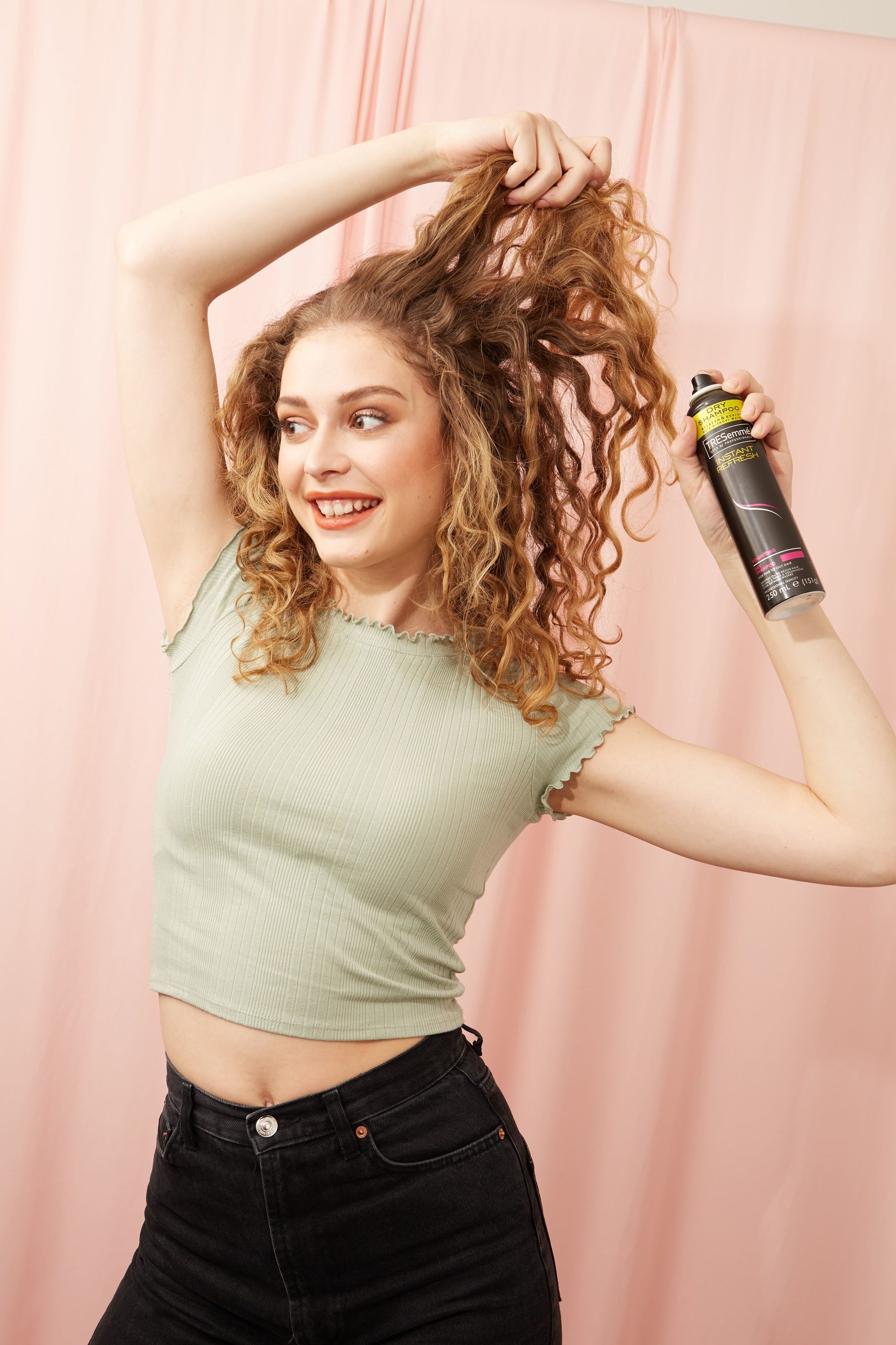 Woman with curly blonde hair spraying dry shampoo