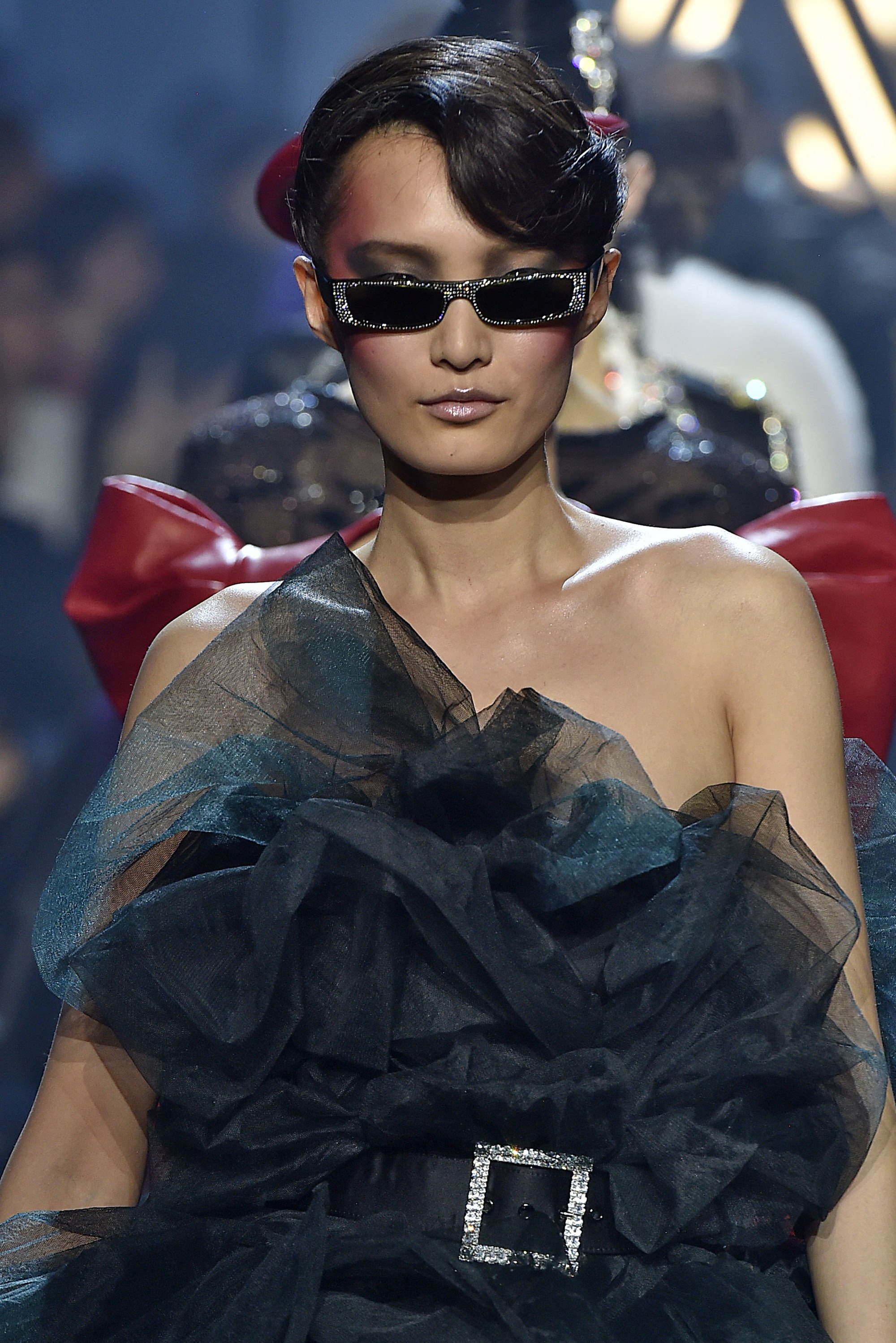 model with brown hair in elegant updo wearing small sunglasses on runway