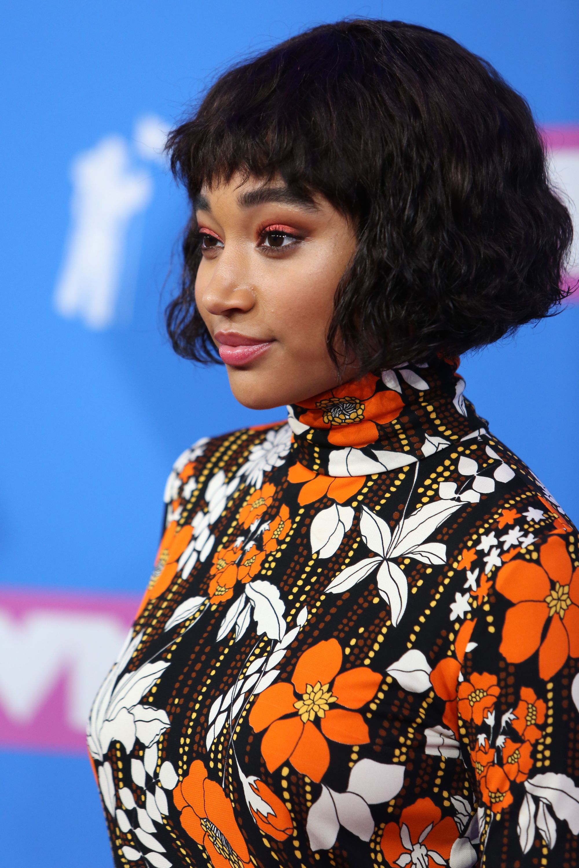 Angled bob: Amandla Stenberg with a short wavy bob with micro bangs, wearing a high neck floral patterned dress