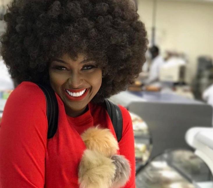 close up shot of amara la negra with big power afro hairstyle, wearing red jumper and posing in a shop