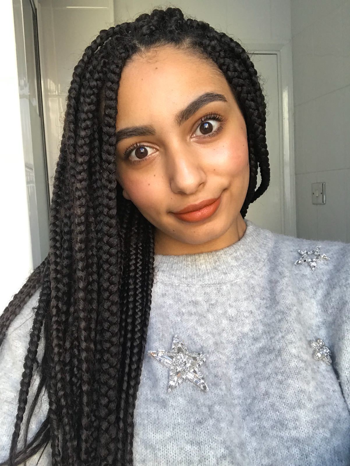 All Things Hair editor Amra with long box braids, swept to the side and wearing a silver jumper