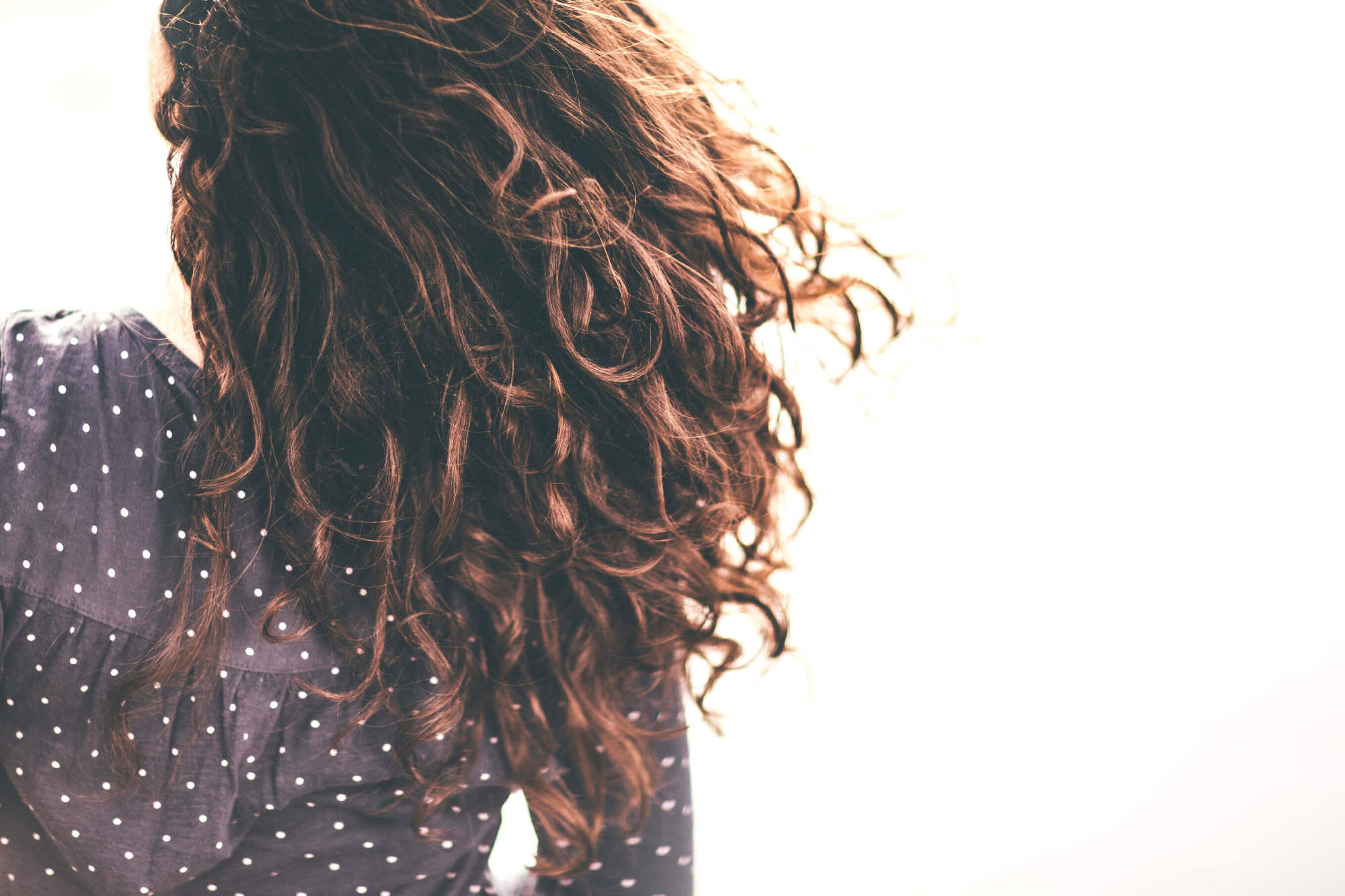 Permed hair care back of woman's head with brunette curly hair