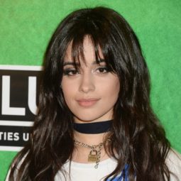 long layered haircuts with bangs: close up of camila cabello with with wispy bangs and shaggy layered hairstyle, wearing white top on the red carpet