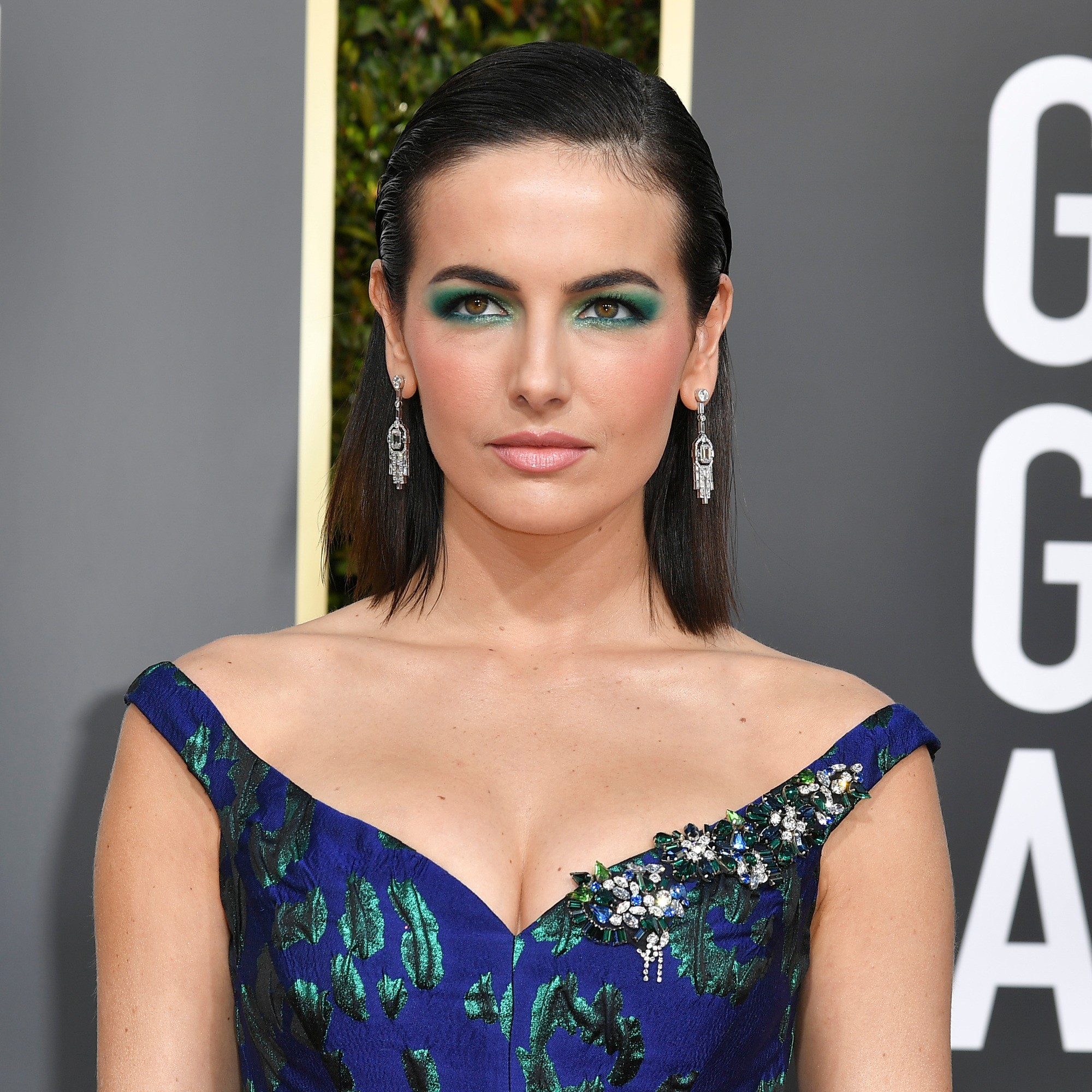 Camilla Belle with slicked back shoulder length dark brown hair, wearing blue gown with green flowers at the 2019 Golden Globes awards ceremony